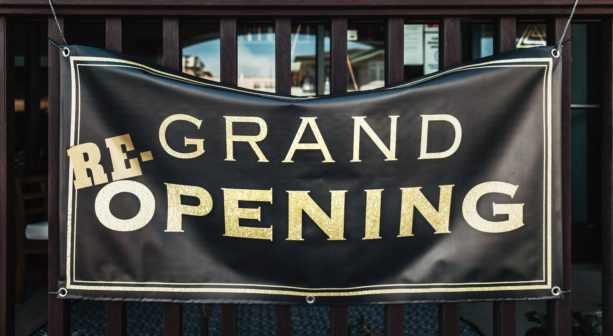 A black banner hanging by grommets with uppercase gold text, reading RE-GRAND OPENING