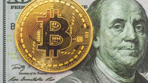A gold coin with the Bitcoin logo over a 100 dollar bill featuring Benjamin Franklin